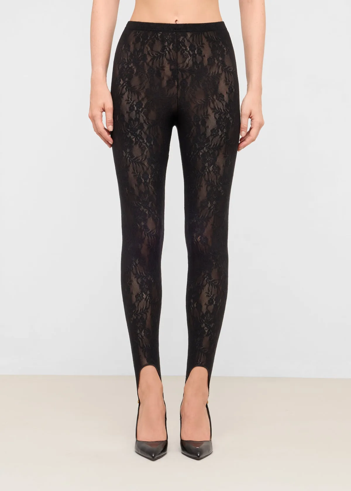 Leggings con staffa in pizzo nero a fiori su una modella, vista frontale, con décolleté a punta di vernice nera