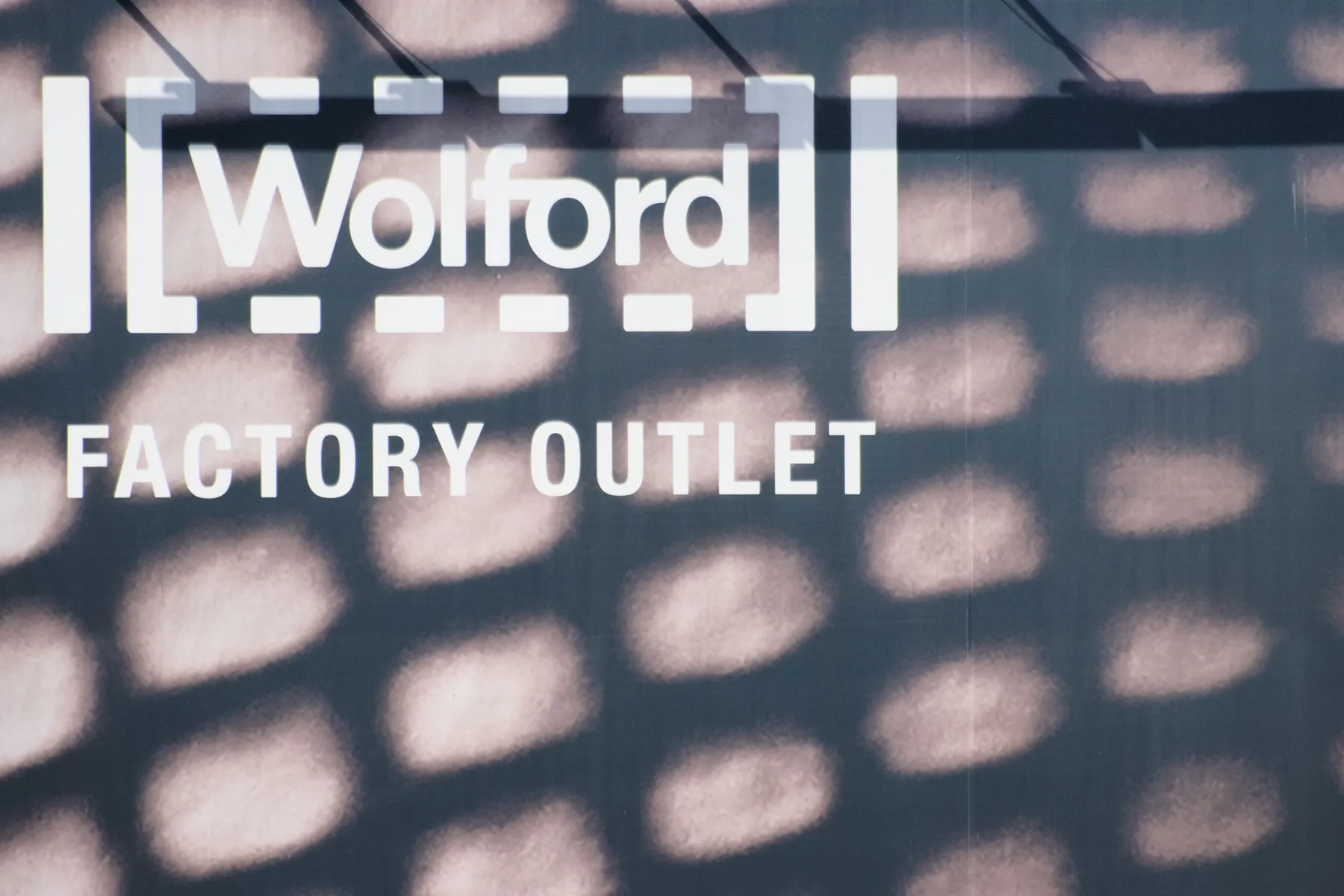 L'insegna del Factory Outlet Wolford a Bregenz, con il logo tra parentesi quadre e l'ombra della facciata traforata