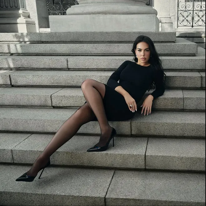 Georgina Rodríguez sdraiata su una scalinata di pietra con un abito nero corto a maniche lunghe, collant velati neri e décolleté nere di vernice