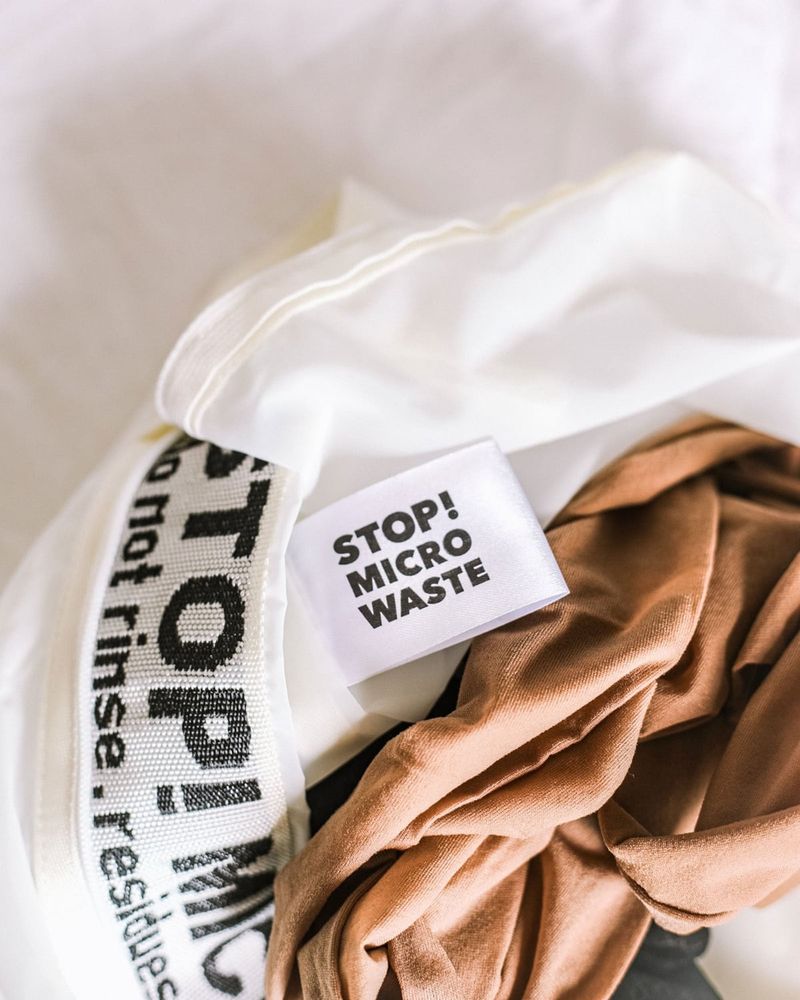 Nude tights next to an open white Guppyfriend washing bag with the label STOP! MICRO WASTE