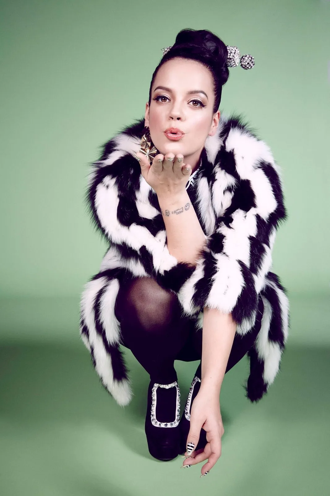 Lily Allen kneeling in a black-and-white striped fur coat, black tights and bow shoes