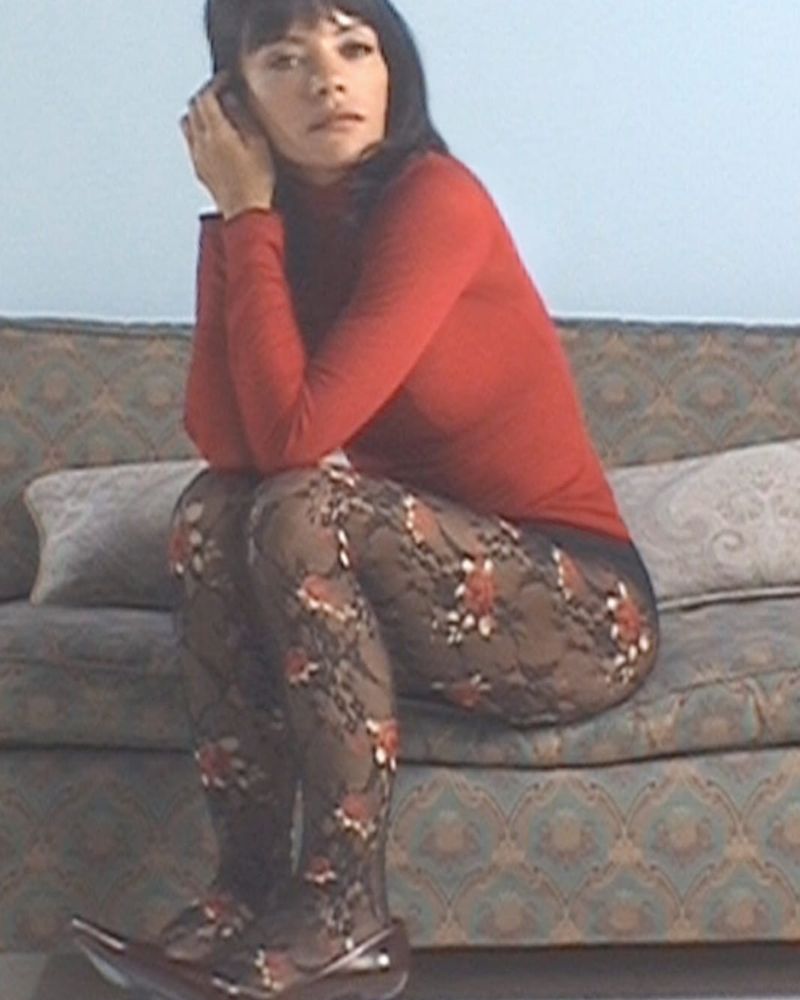 Lily Allen sitting on a sofa in a red roll-neck, Calzedonia Liberty floral fishnet tights and black pumps, in the Autumn/Winter 2026 campaign
