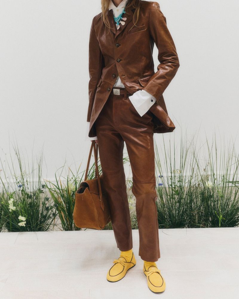 Look 10 from Polo Ralph Lauren spring/summer 2027, a brown leather coat and trousers, yellow ribbed socks and yellow loafers, a suede bag
