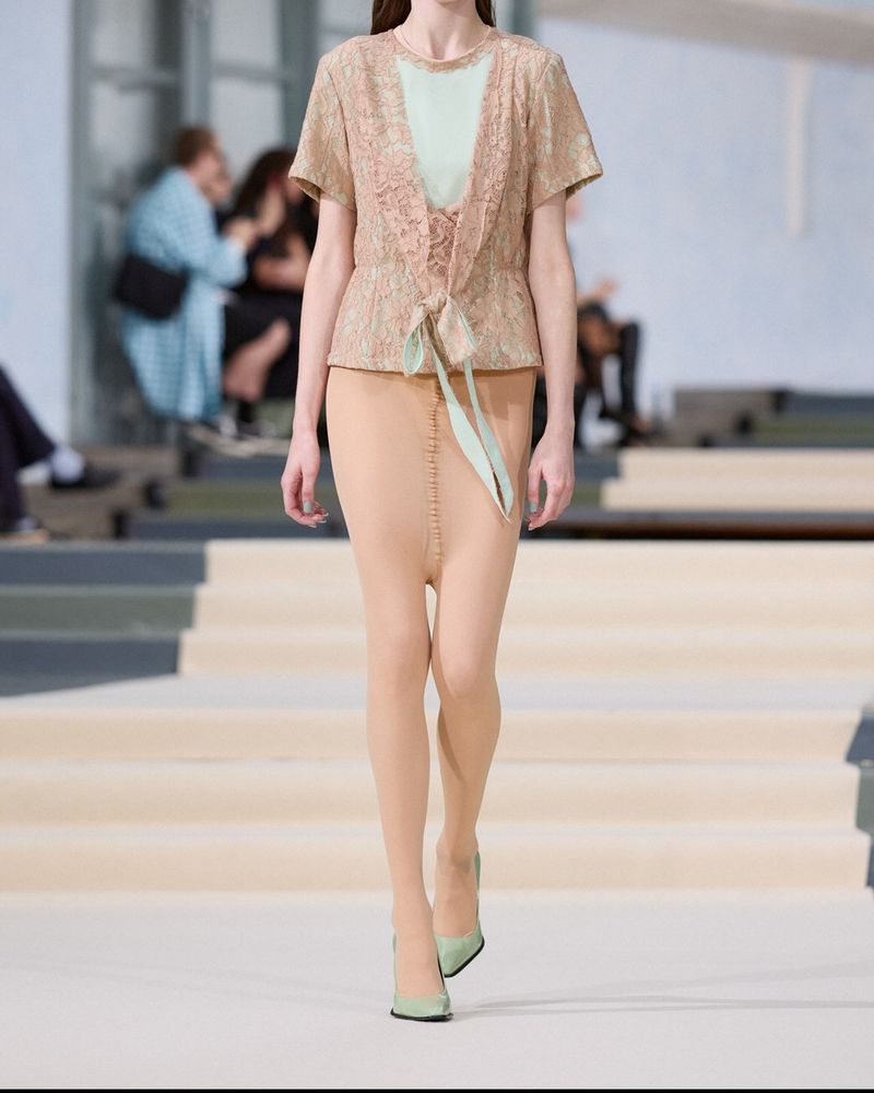Runway look 12 from Julie Kegels spring/summer 2027, nude tights worn under a short lace-trimmed jacket tied with a mint ribbon