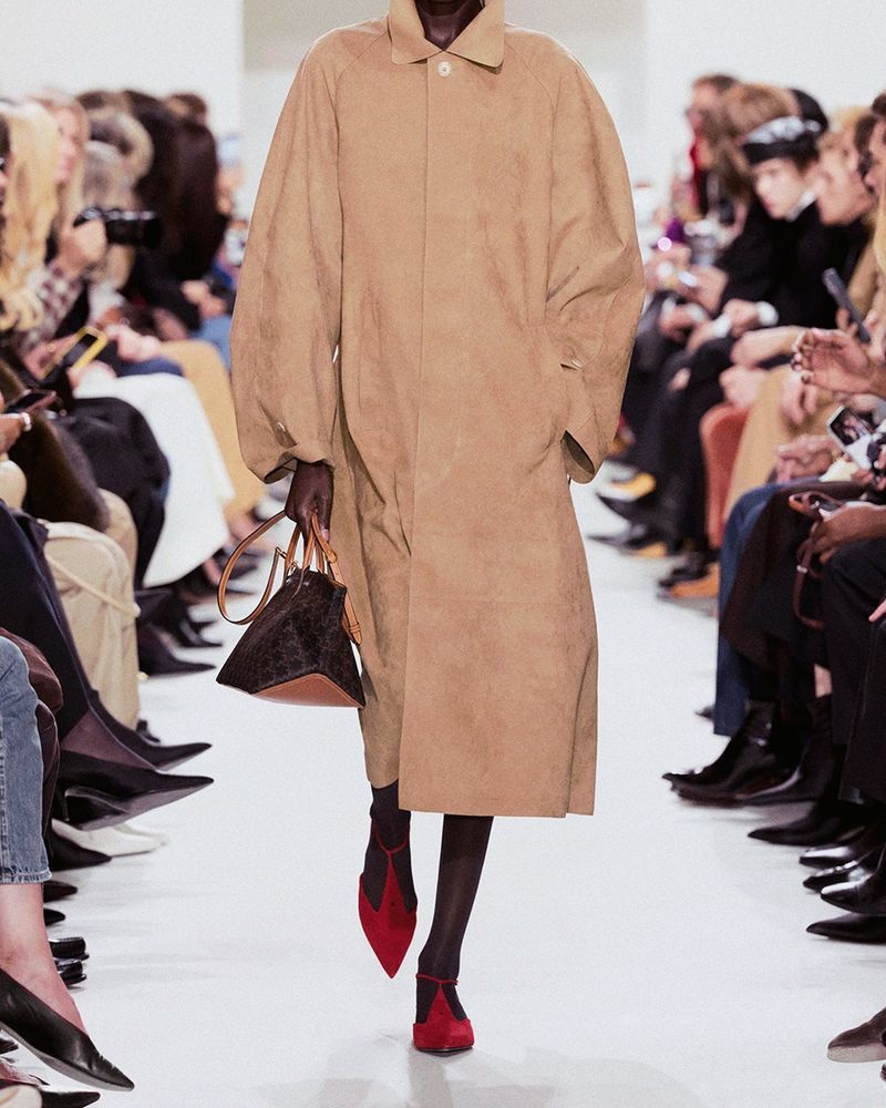 Runway look 20 from Celine spring/summer 2027, sheer black tights and red suede pointed pumps with an ankle strap under a long camel suede coat