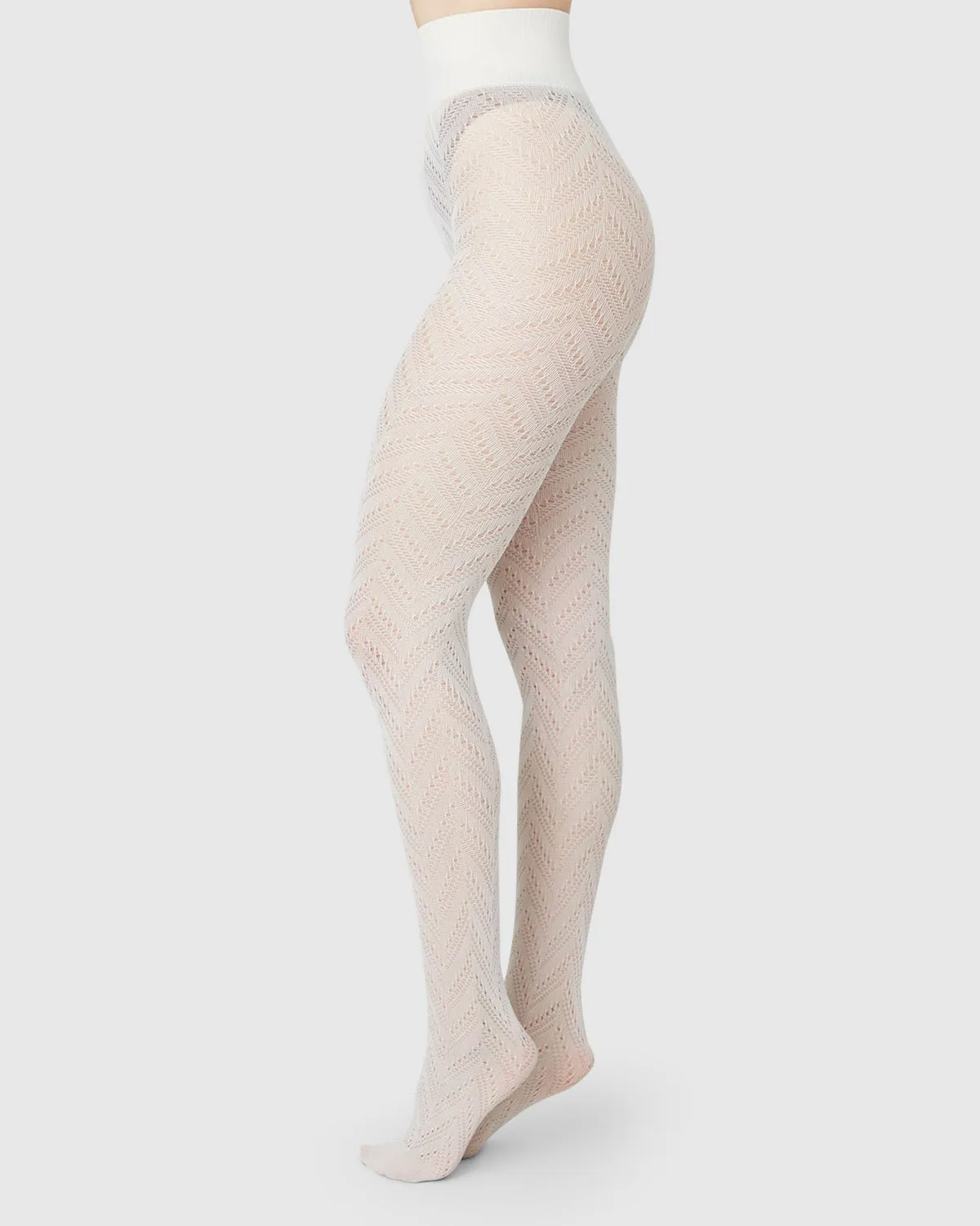 Gambe in collant avorio traforati a spina di pesce con un'alta fascia in vita in maglia, su fondo grigio