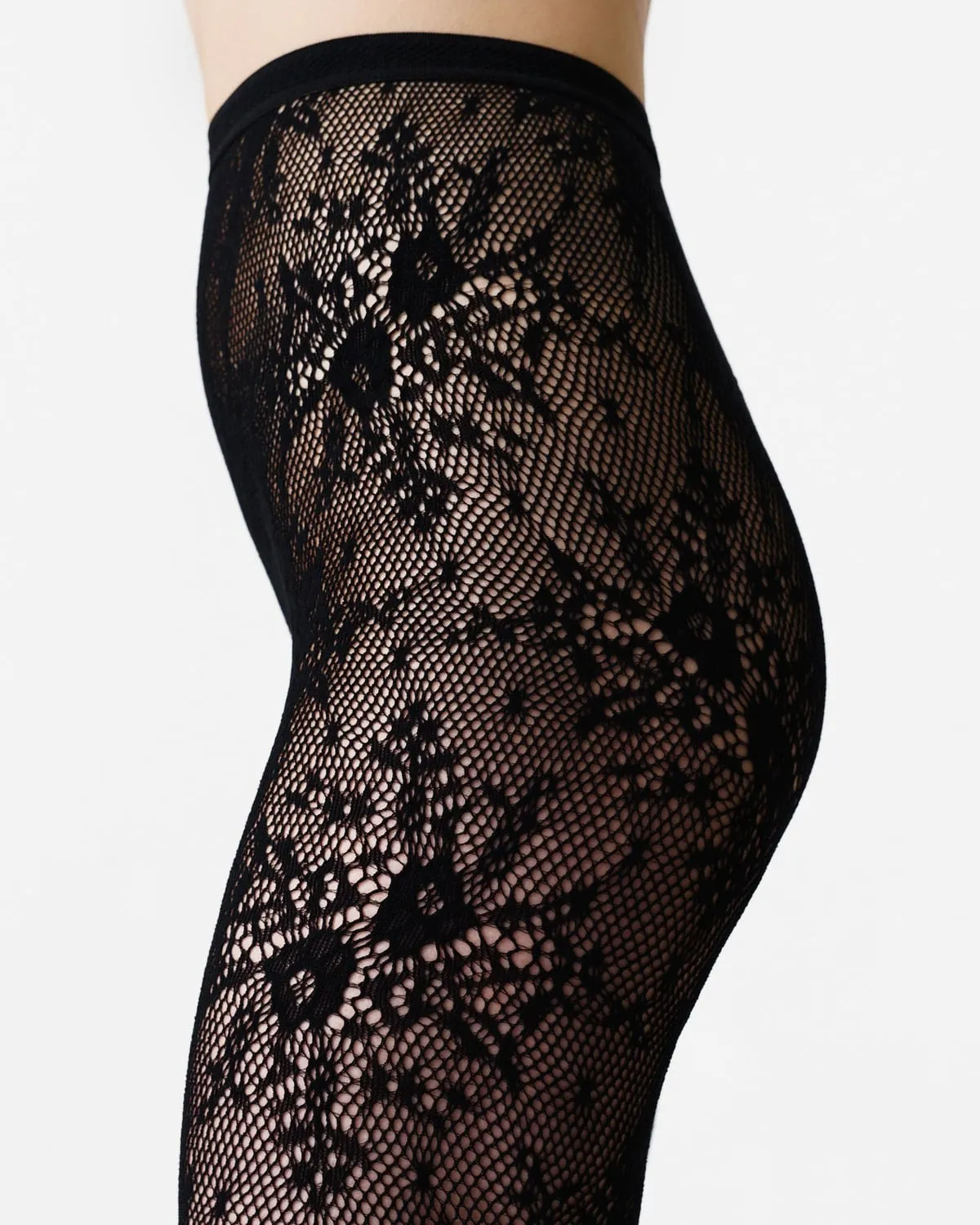 Close-up of black floral lace tights on the hip and thigh, Swedish Stockings Rosa Lace Tights
